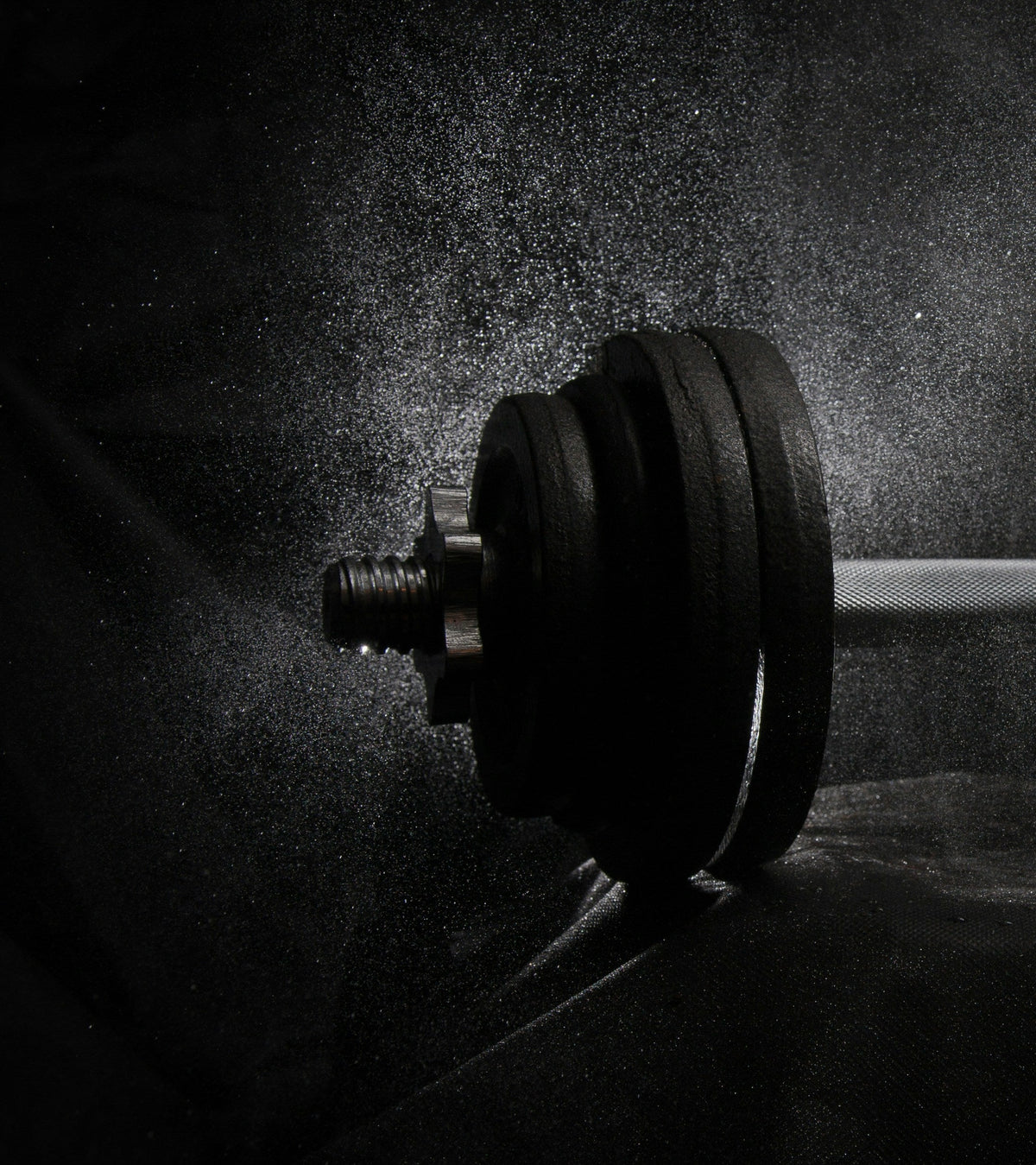 A loaded dumbbell in low light with fine chalk dust in the air, for an article on why pre-workout makes you itch