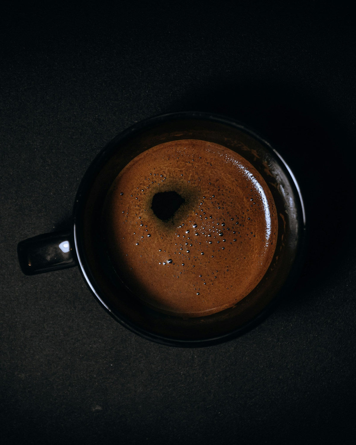 A black mug of coffee on a dark table seen from above, for an article on paraxanthine and caffeine