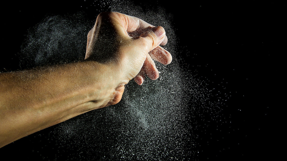 A hand releasing a cloud of lifting chalk against a black background, for an article on how much protein per day to build muscle