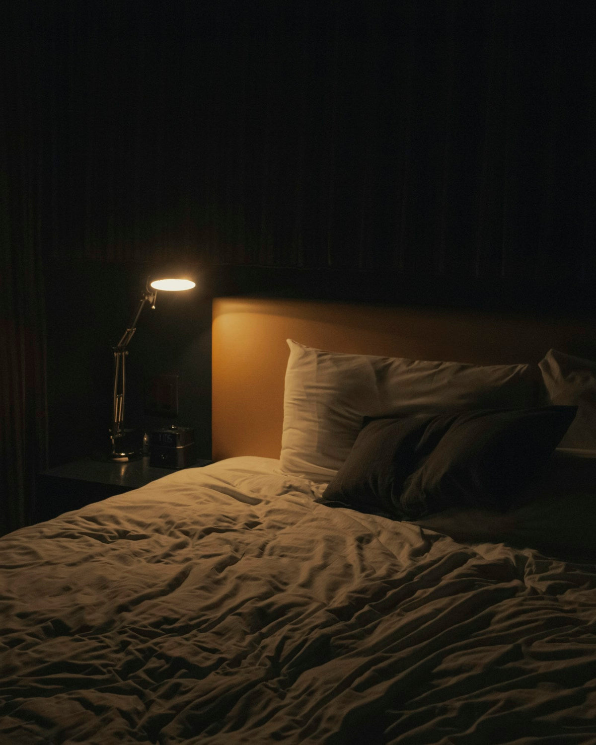 A dark bedroom lit by a single soft bedside lamp, illustrating research on ashwagandha and sleep
