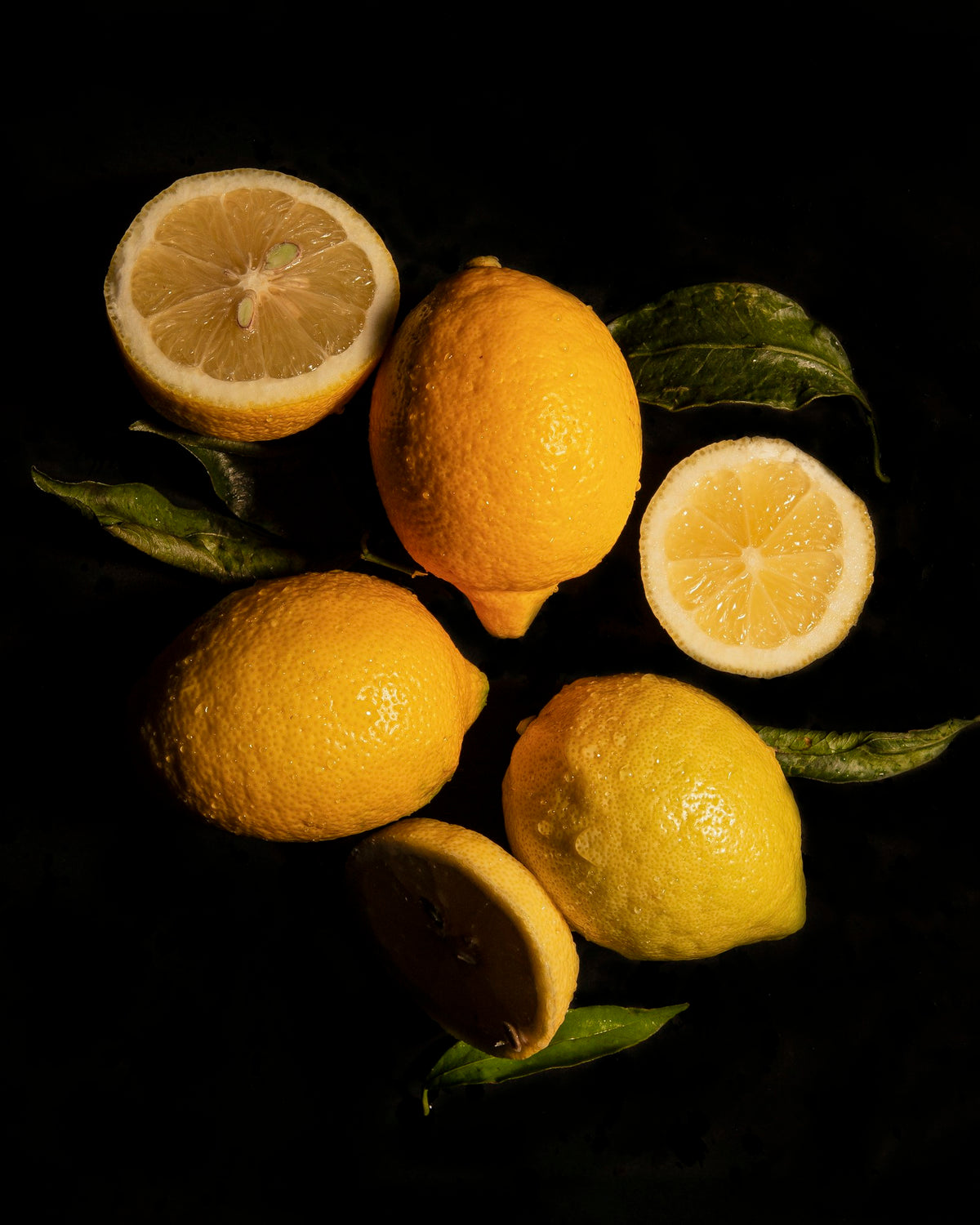 Whole and halved lemons with leaves on a black background
