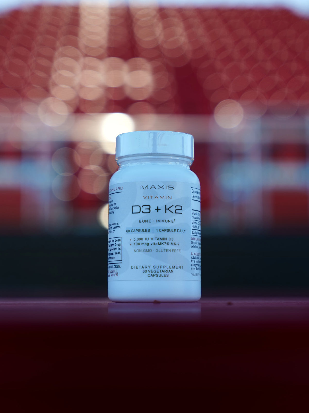 MAXIS Vitamin D3 + K2, bottle on a ledge in front of stadium seats